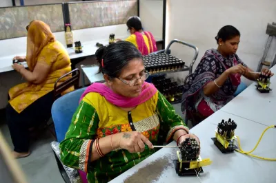 Women with disabilities in India sitting at tables working with screwdrivers on electric gadgets.