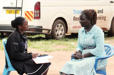 Two women sitting down in plastic chairs, one listening to the other speak.