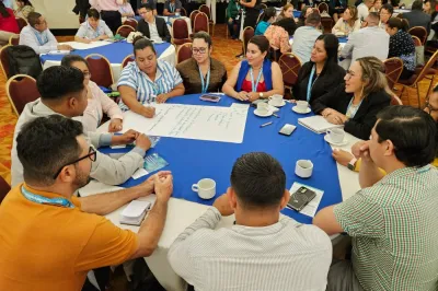 Group of workshop participants sitting around a table discussing and writing ideas on large paper.