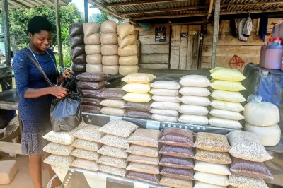 Ghanaian woman vendor at shop with many plastic bags of grains piled up.