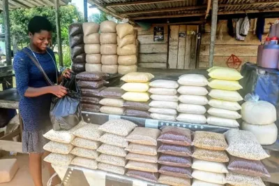Commerçante ghanéenne dans une boutique, avec de nombreux sacs plastiques de céréales empilés.