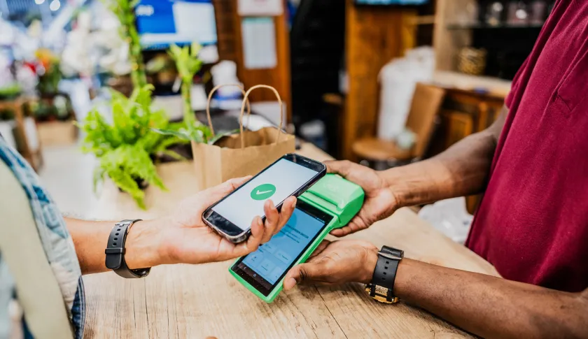 Dos personas sostienen un celular y un datáfono en el momento de efectuar una transacción digital.