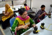 Women with disabilities in India sitting at tables working with screwdrivers on electric gadgets.