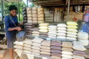 Ghanaian woman vendor at shop with many plastic bags of grains piled up.