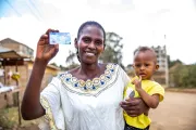 Woman with child in her arms holding up an ID card and smiling.