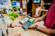 Dos personas sostienen un celular y un datáfono en el momento de efectuar una transacción digital.